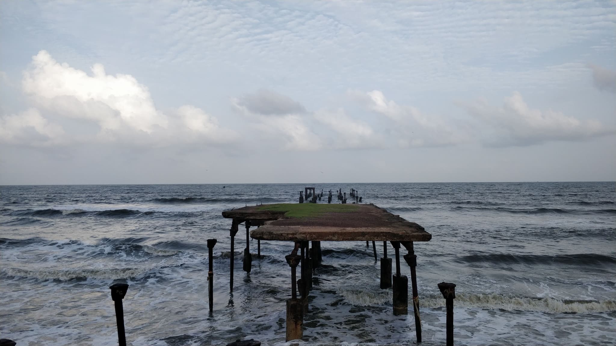 Old abandoned pier standing in rough seas with cloudy sky