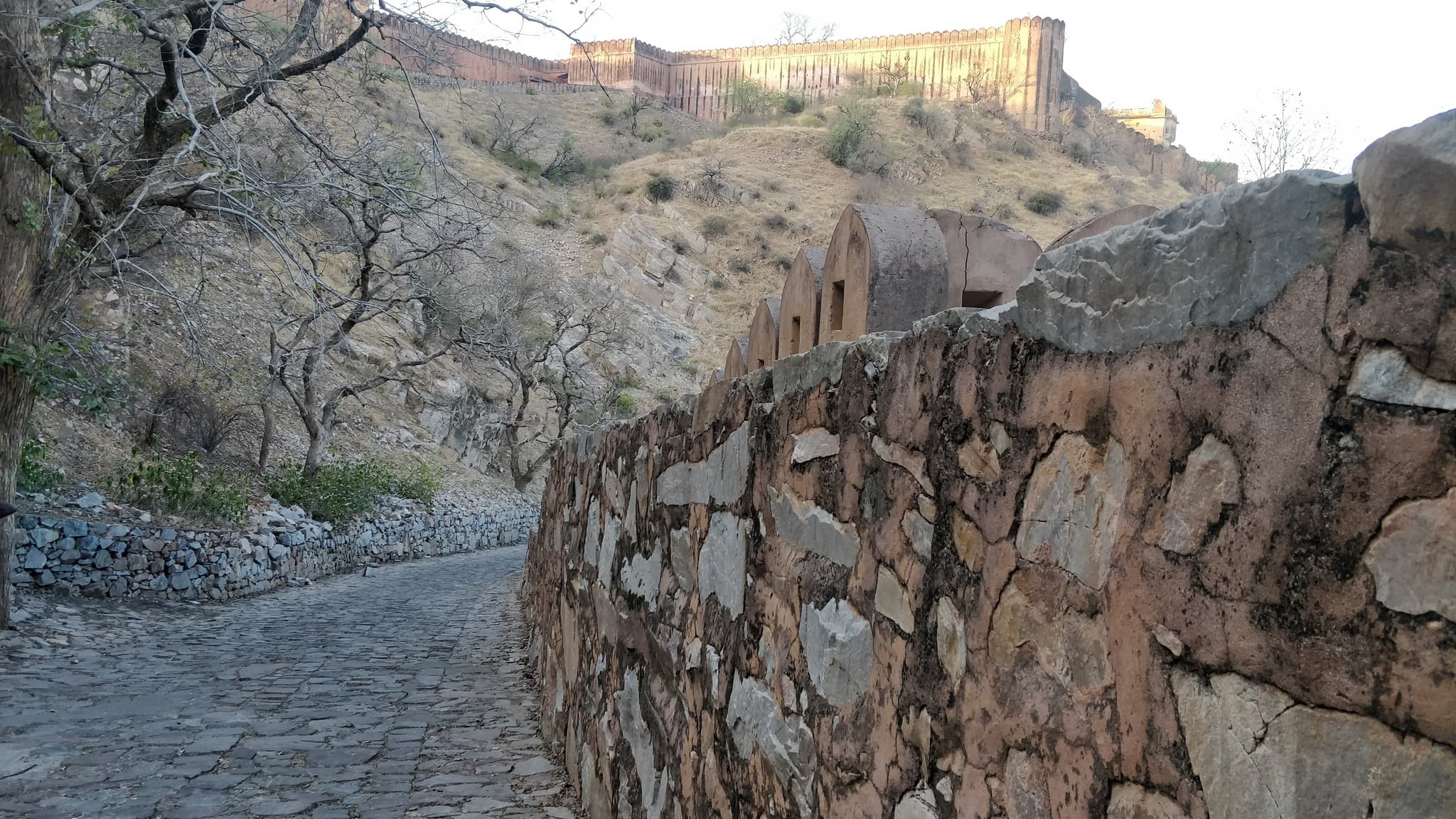 Stone wall path leading uphill to a fort in golden hour light