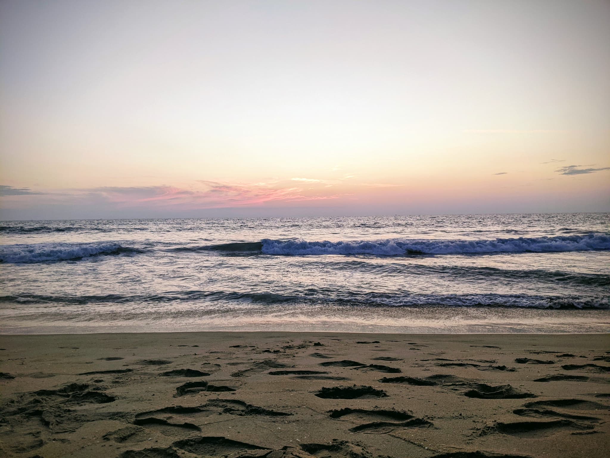 Subdued beach sunset with soft pastel tones and gentle waves on the shore