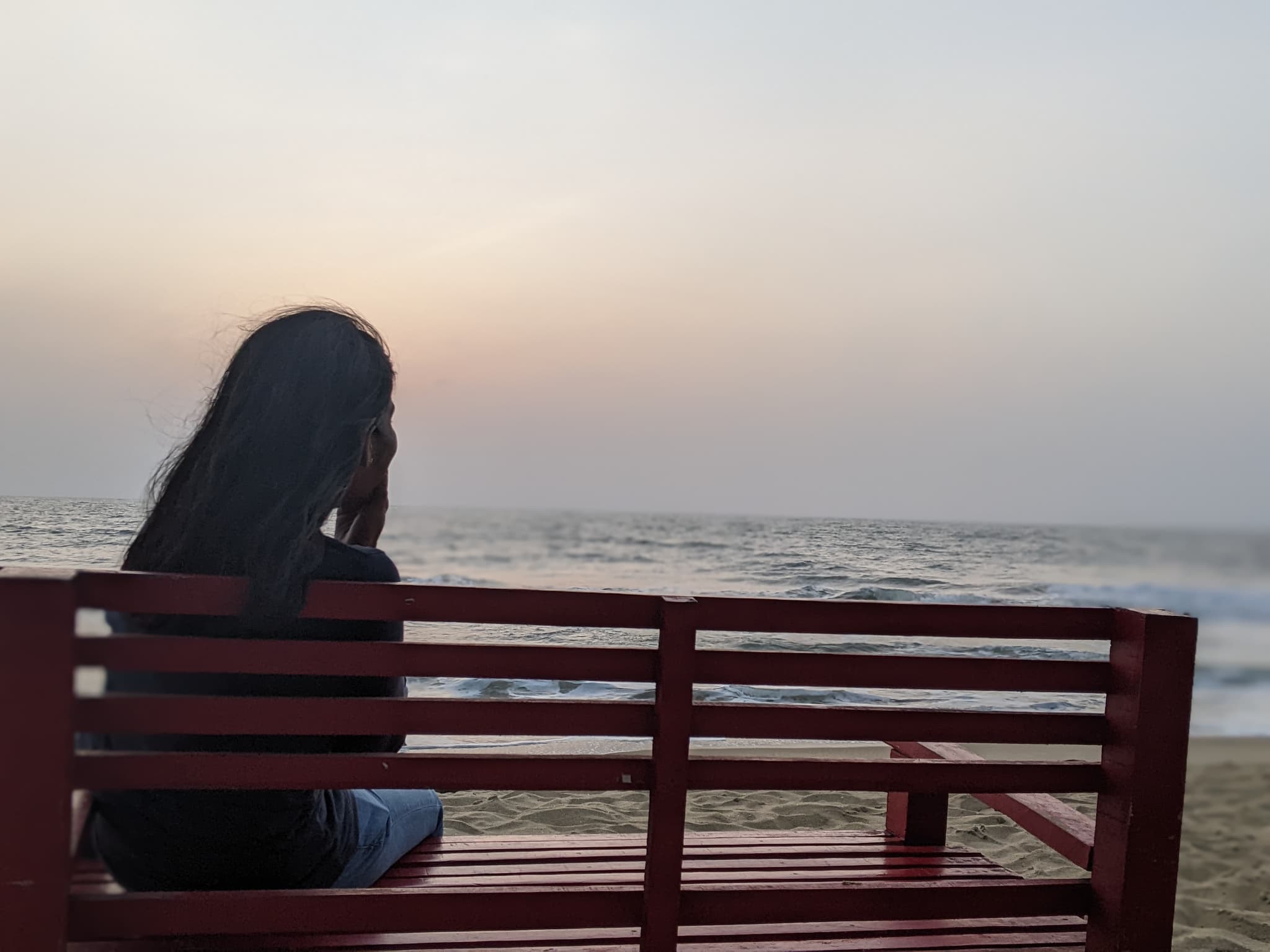 A person sitting on a bench at the edge of the sea, looking out at the water at dusk