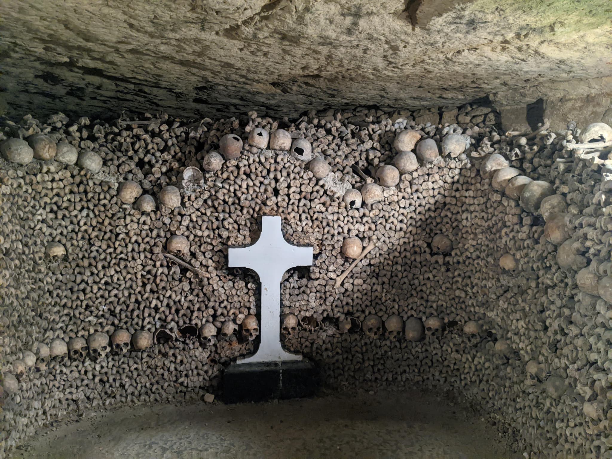 Paris Catacombs interior with skulls and bones arranged around a stone cross
