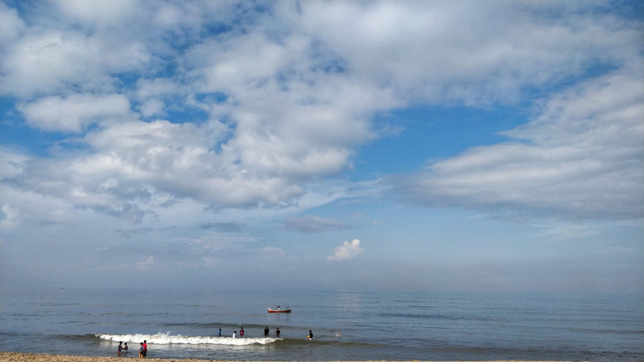 Beach scene with big sky, clouds, waves, and people in water