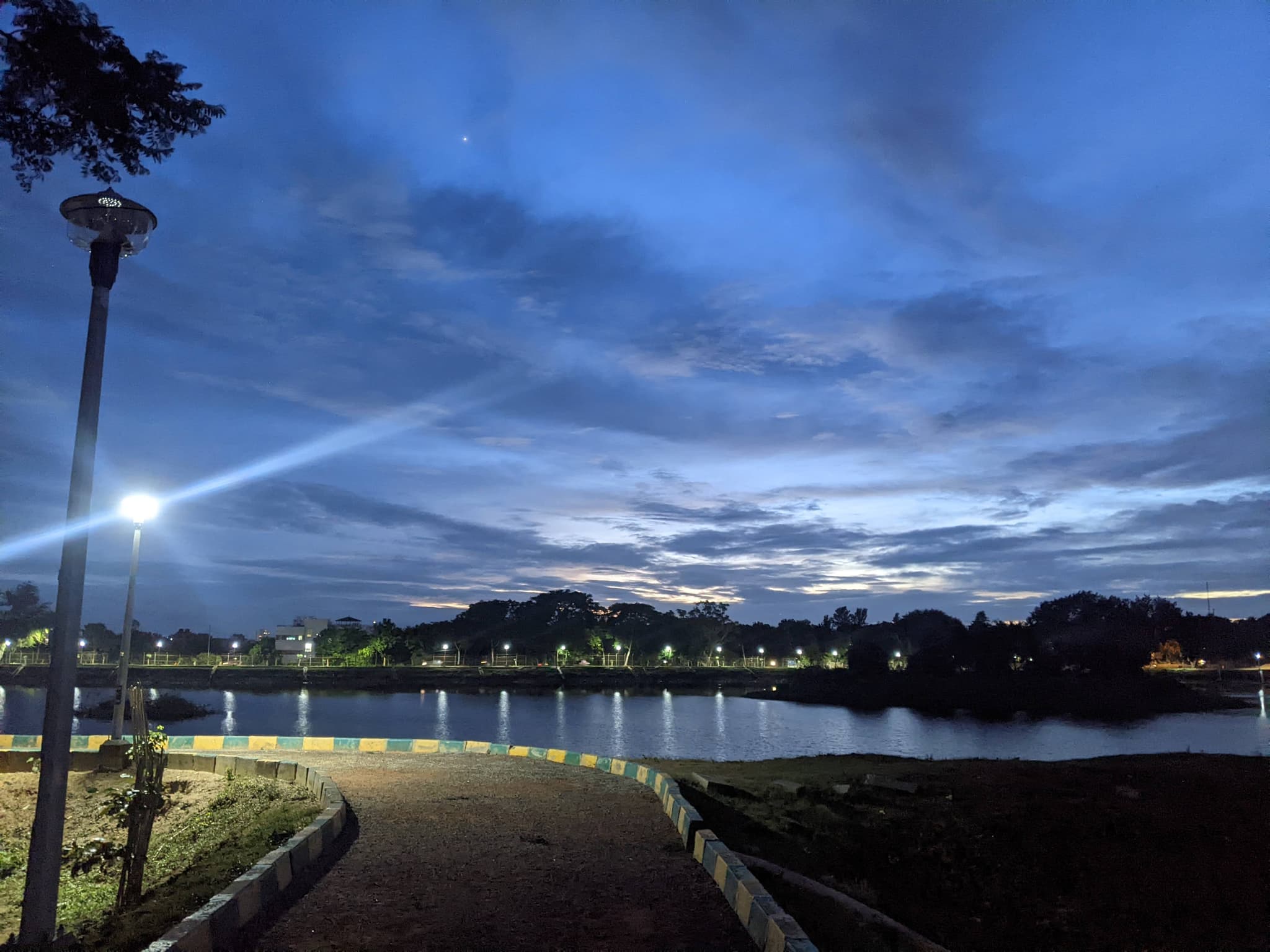 Lake at blue hour with street light reflecting on water, pathway curving alongside