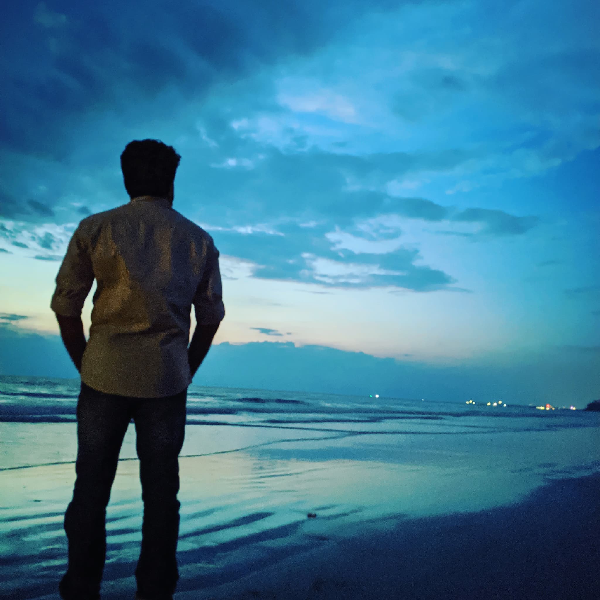 Silhouette of person standing on blue-hour beach looking at dramatic twilight sky