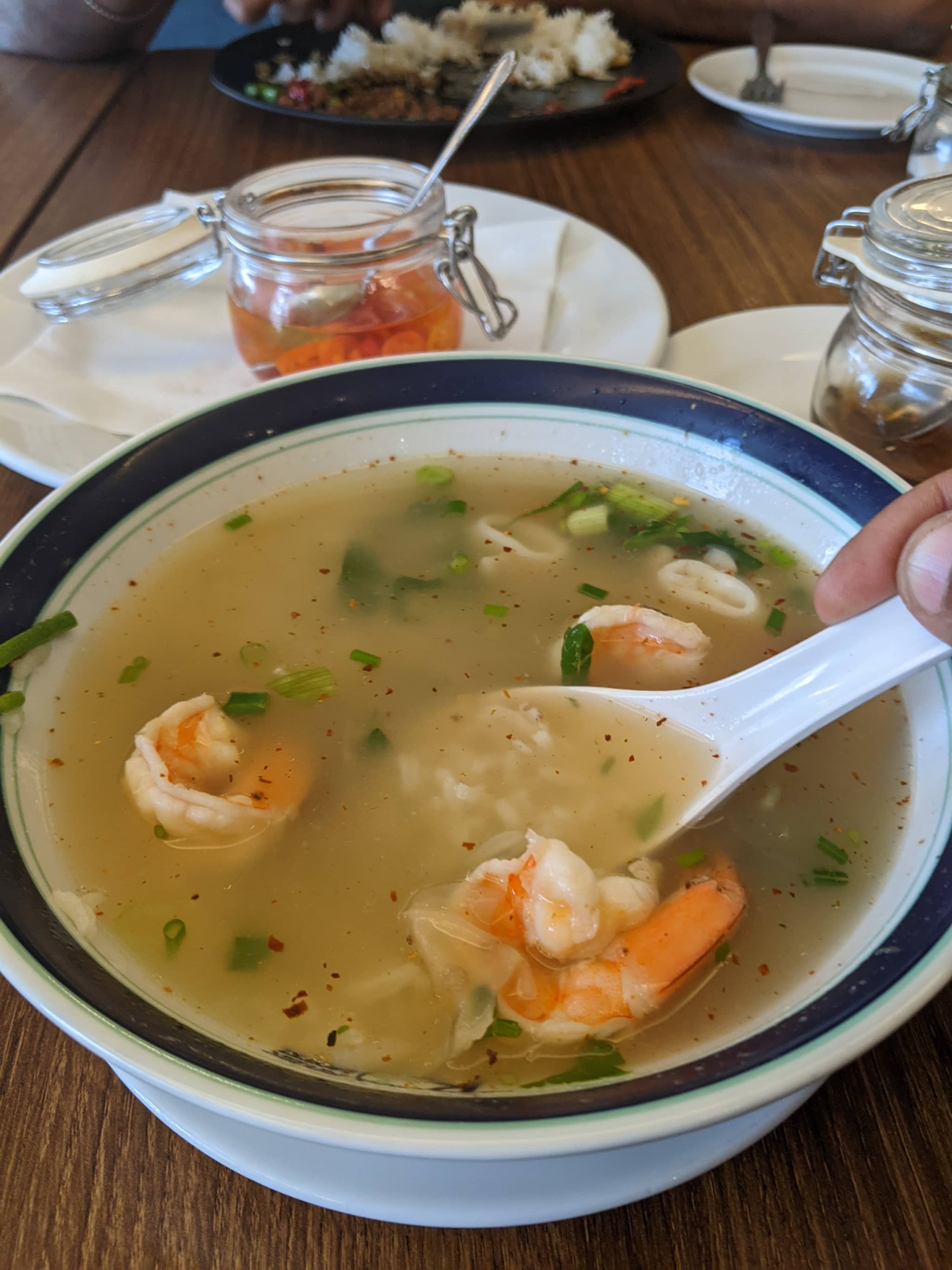 A bowl of prawn wonton soup at a restaurant table with warm lighting
