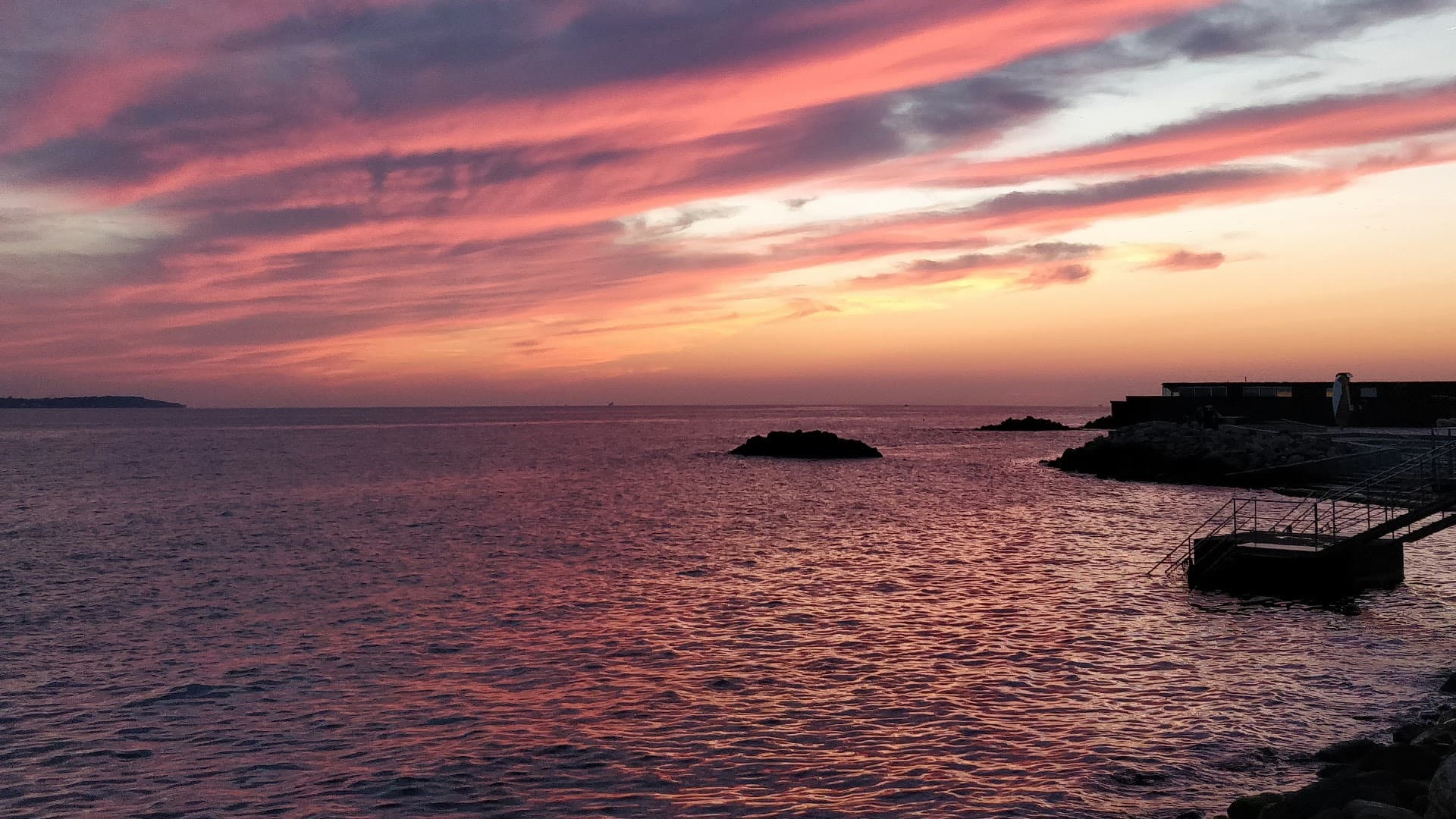 Stunning pink-purple sunset over sea with rocky coastline