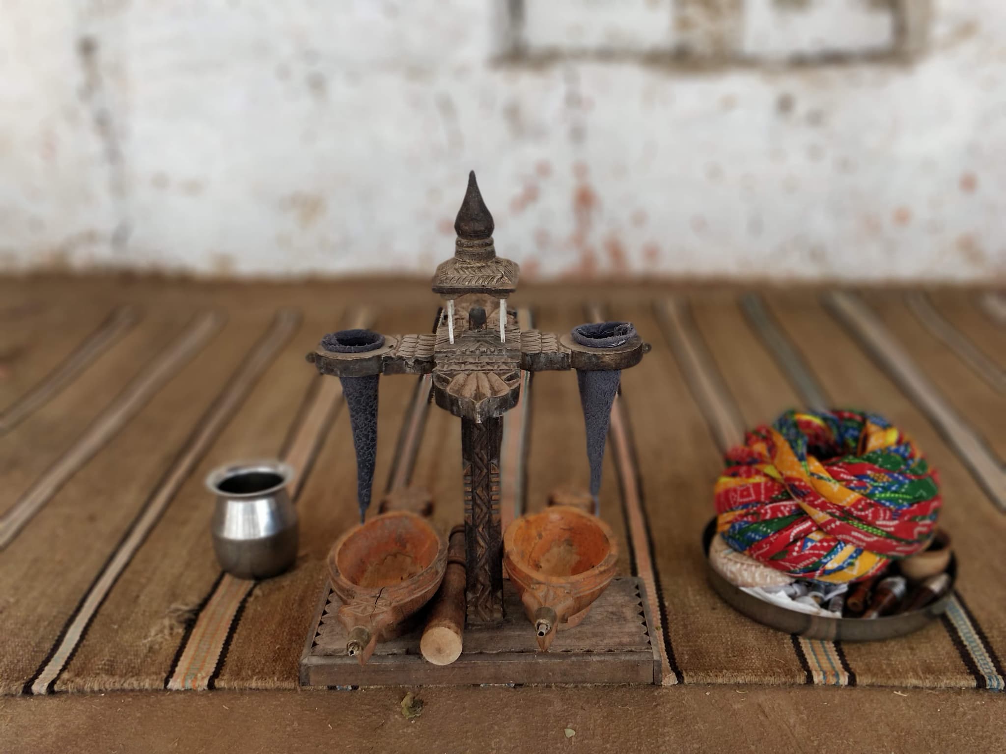 Ornate traditional wooden carved item with small metal pot and colorful turbans