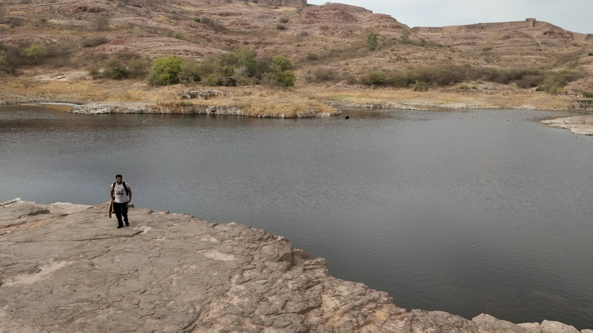 Person standing on rocky outcrop by a desert lake with arid hills behind