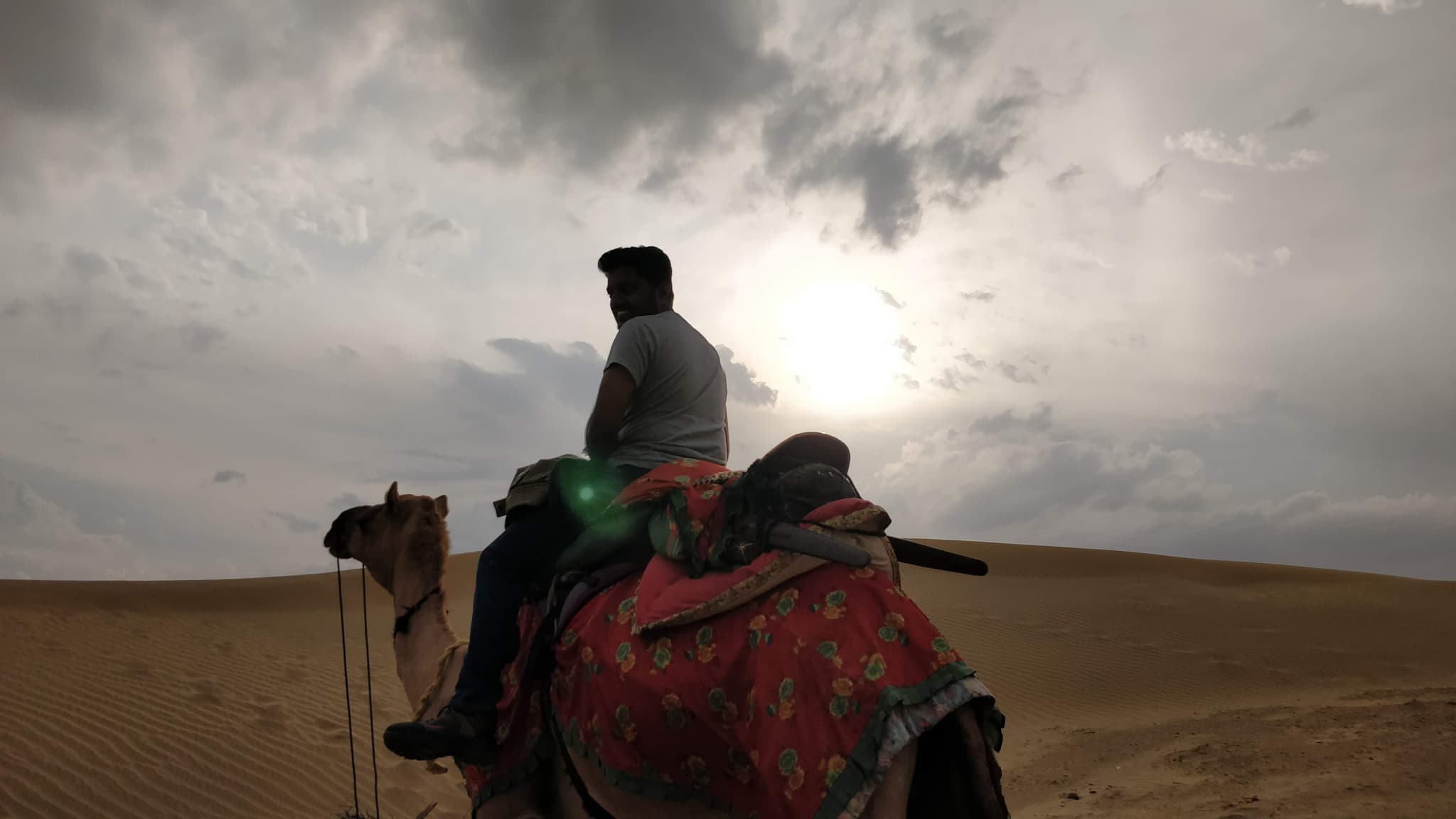 Camel rider silhouetted against dramatic sun and clouds on sand dune