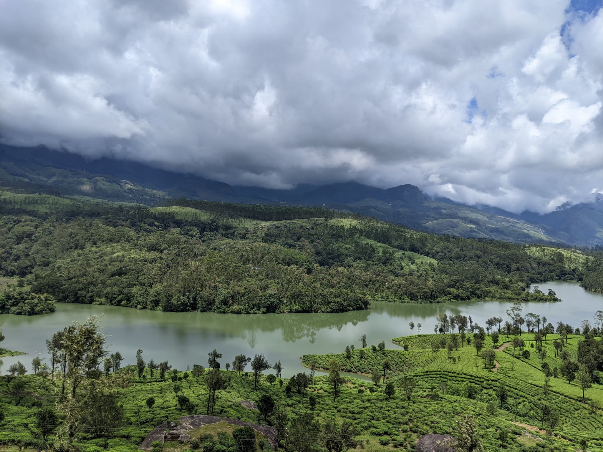 Lake nestled in lush green hills with tea plantations and dramatic clouds