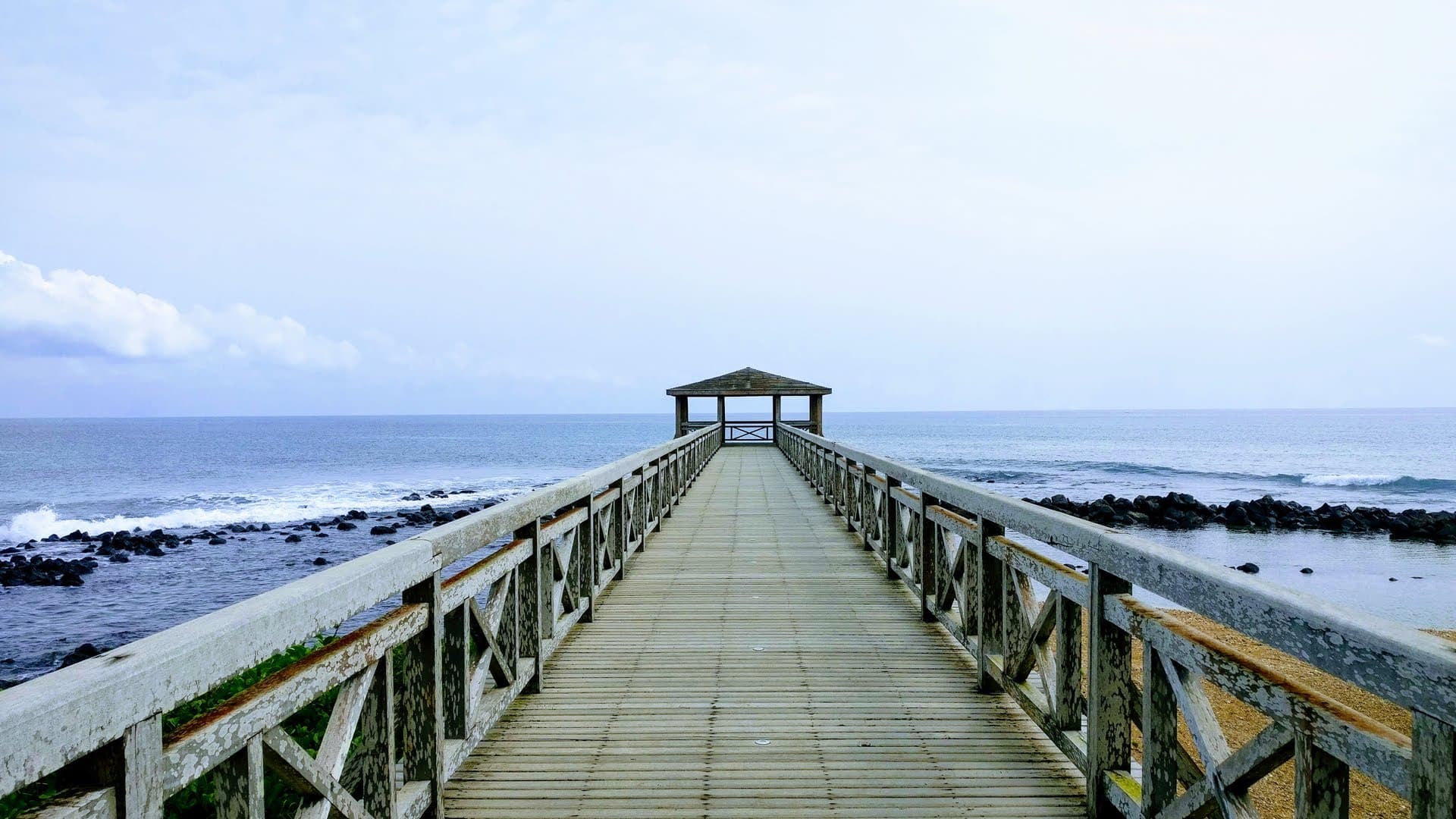 Wooden pier extending into calm ocean with a gazebo at the end