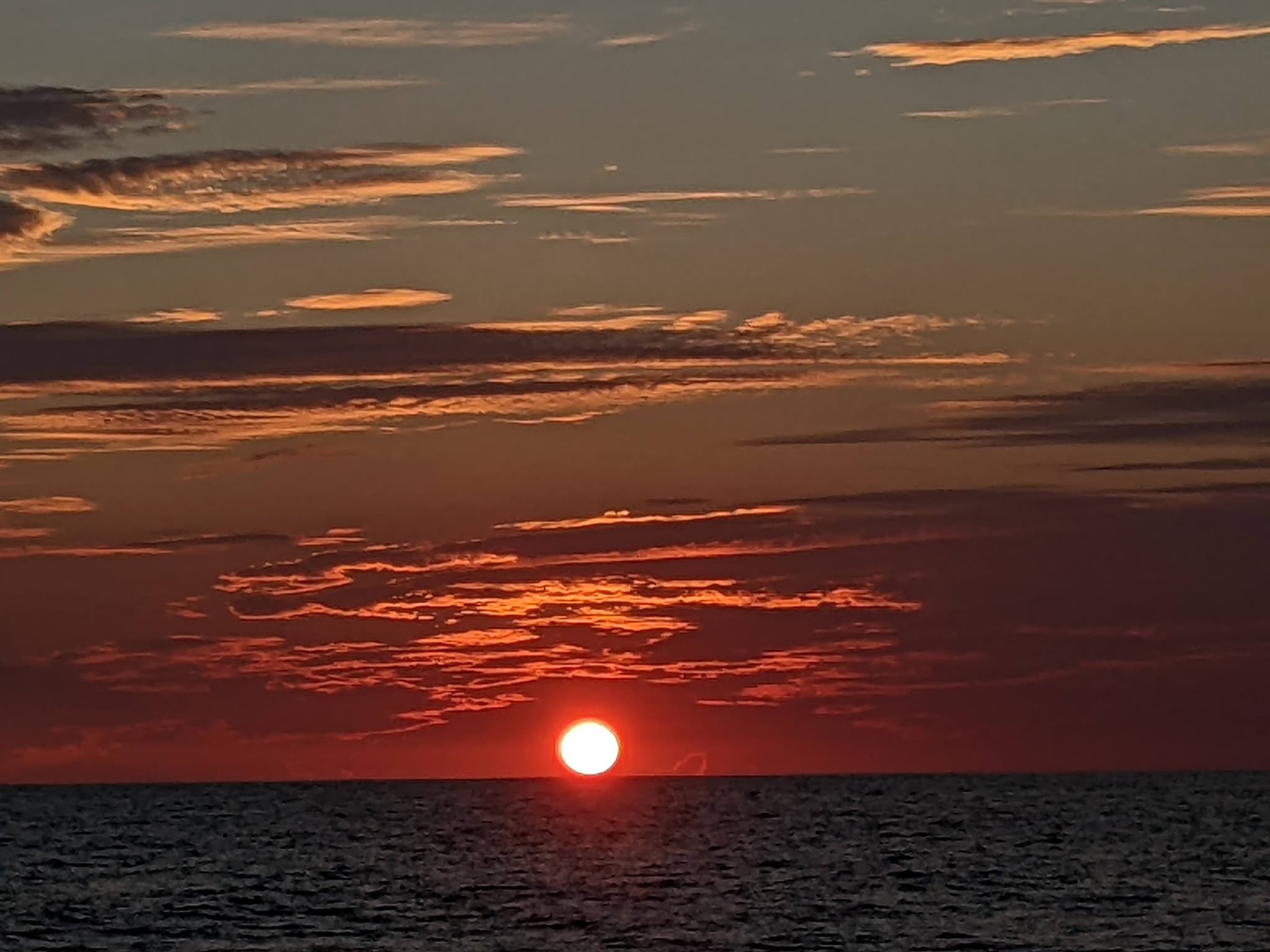The sun touching the ocean horizon, sky streaked with deep reds and oranges