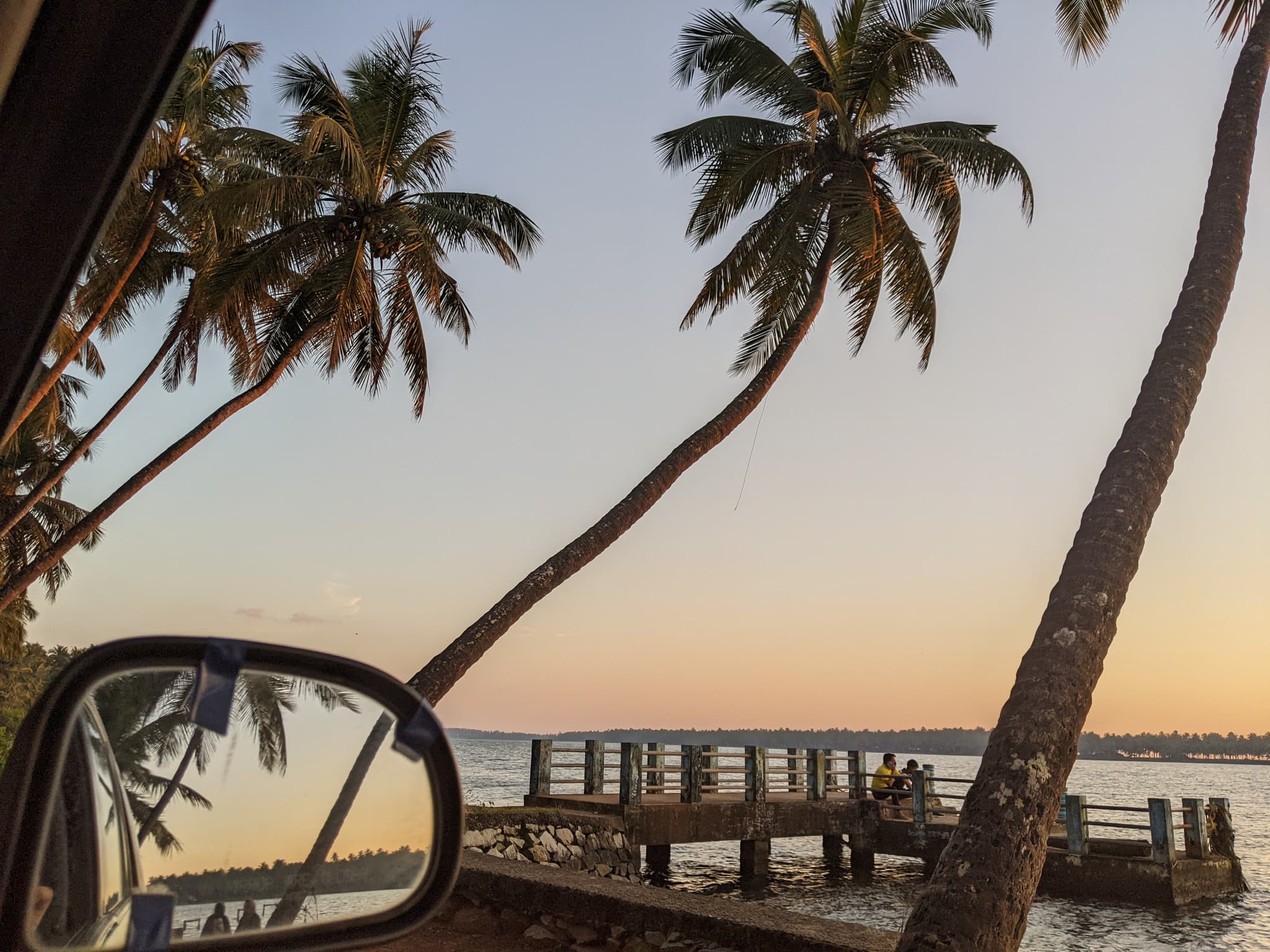 Palm trees and a jetty at sunset, reflected in a car's side mirror