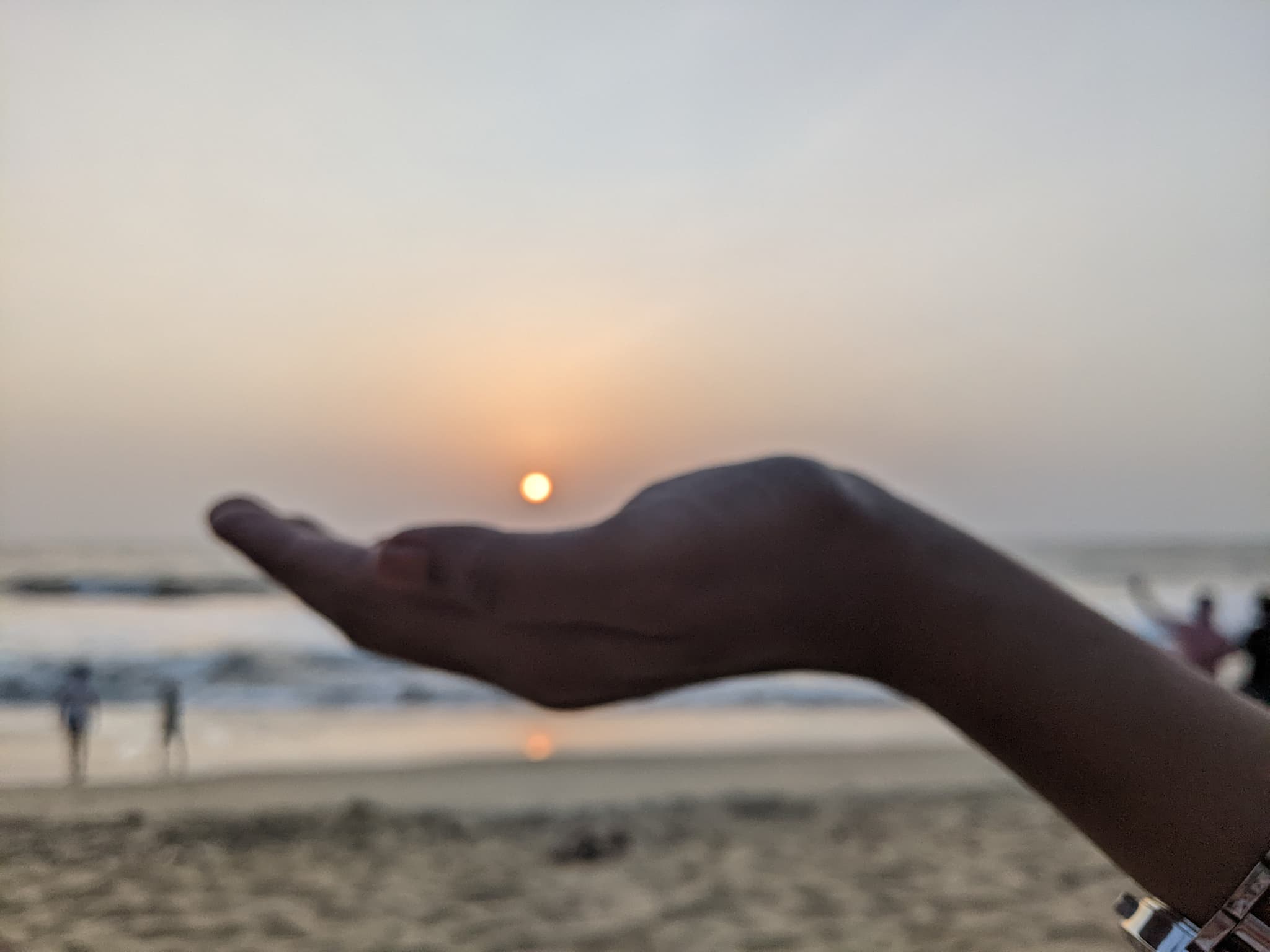 A hand appearing to hold the setting sun on a beach at sunset, creative forced perspective