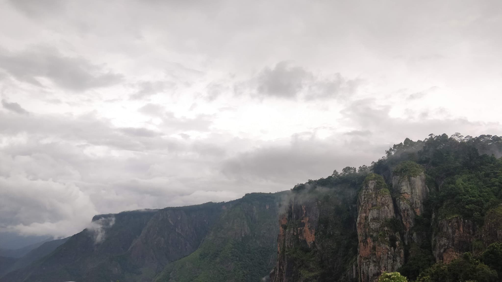 Dramatic cliff face with clouds and lush green vegetation