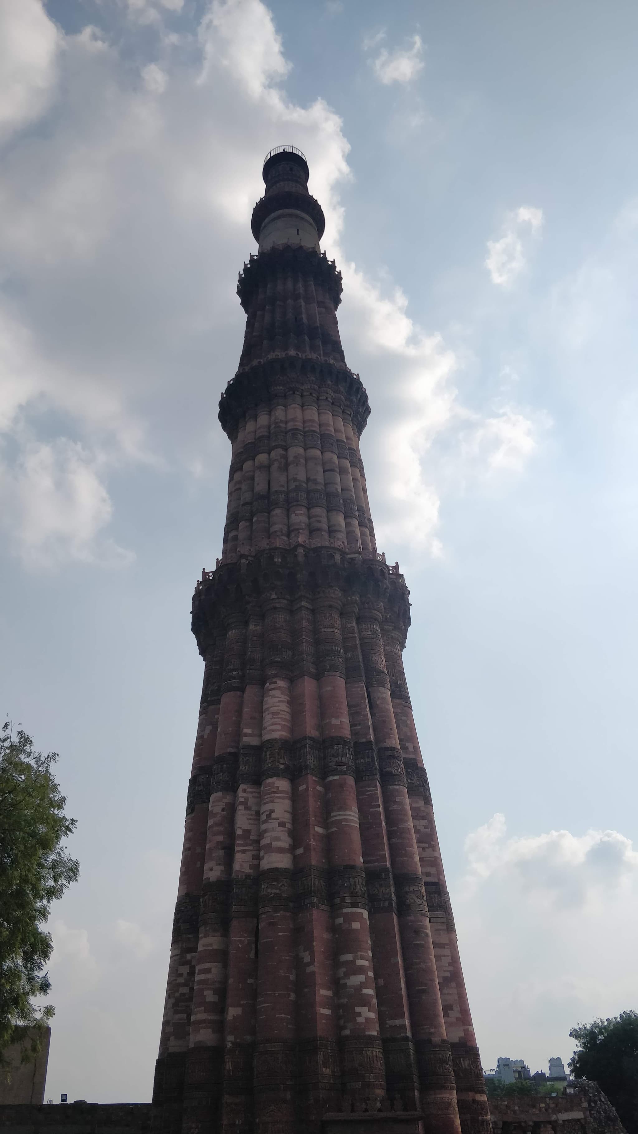 Qutub Minar tower shot from below, dramatic perspective against clouds