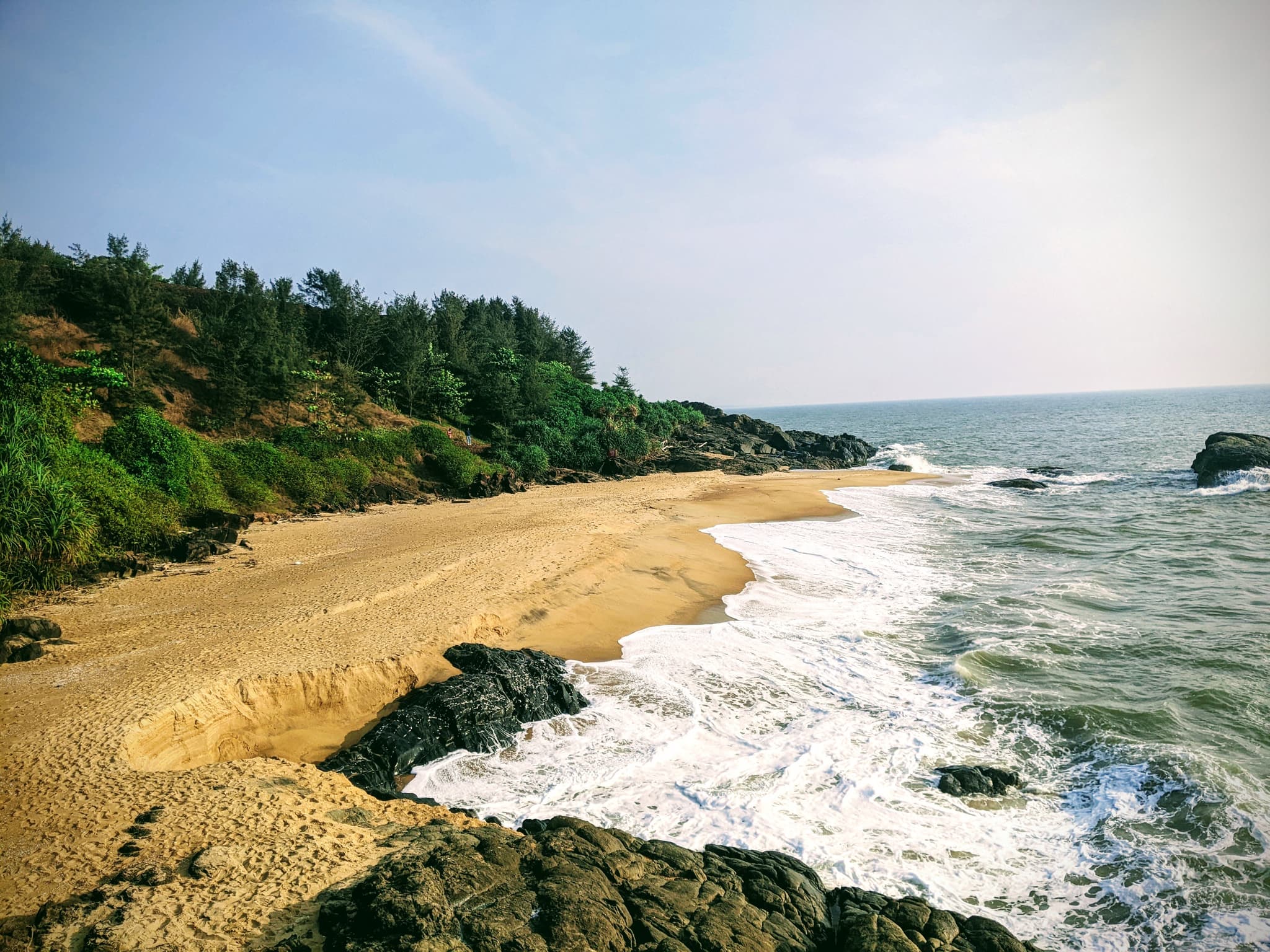 A secluded rocky beach with golden sand and dense trees on the hillside