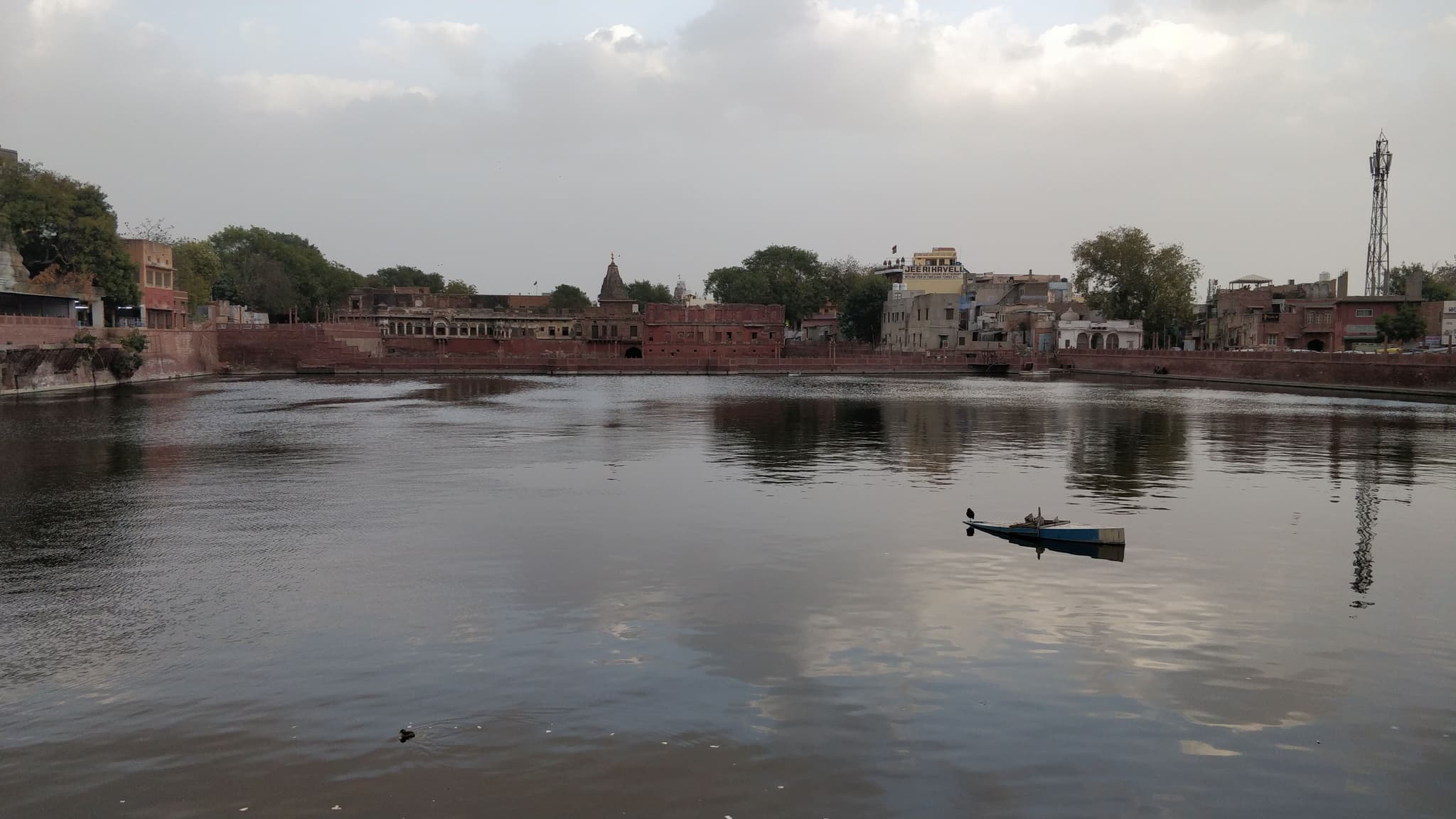 Red sandstone buildings reflected in still lake water with a lone boat