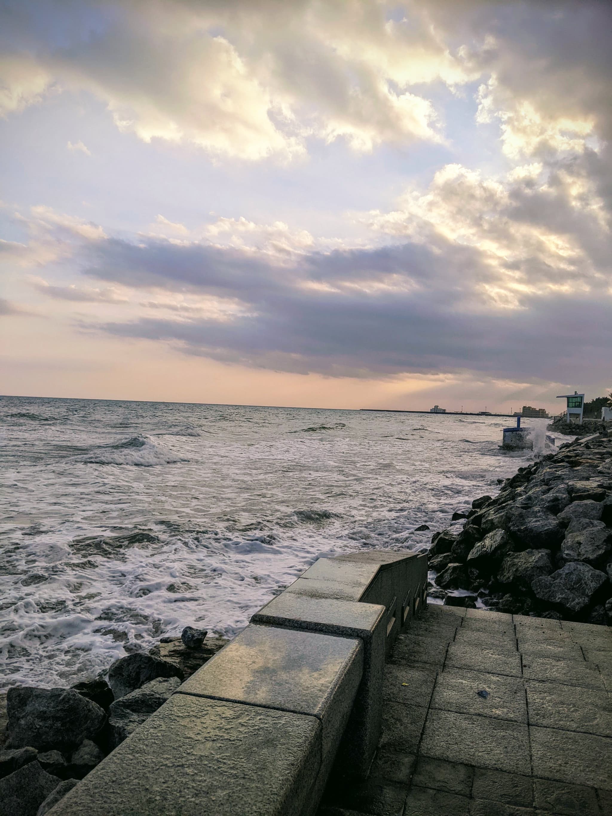 Rocky seashore with waves crashing, dramatic cloudy sky with light breaking through