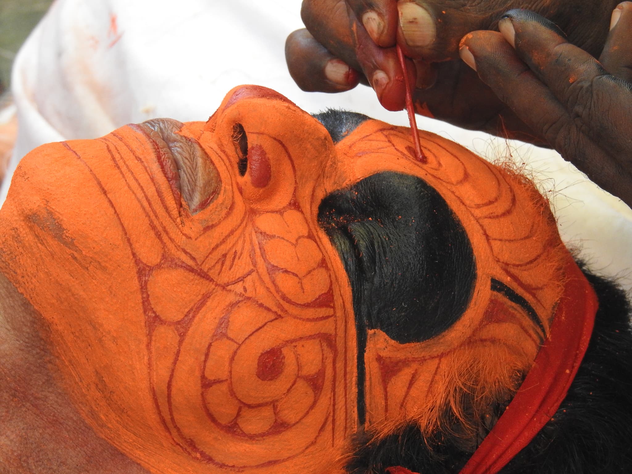 An artist carefully painting intricate patterns on a Theyyam performer's face