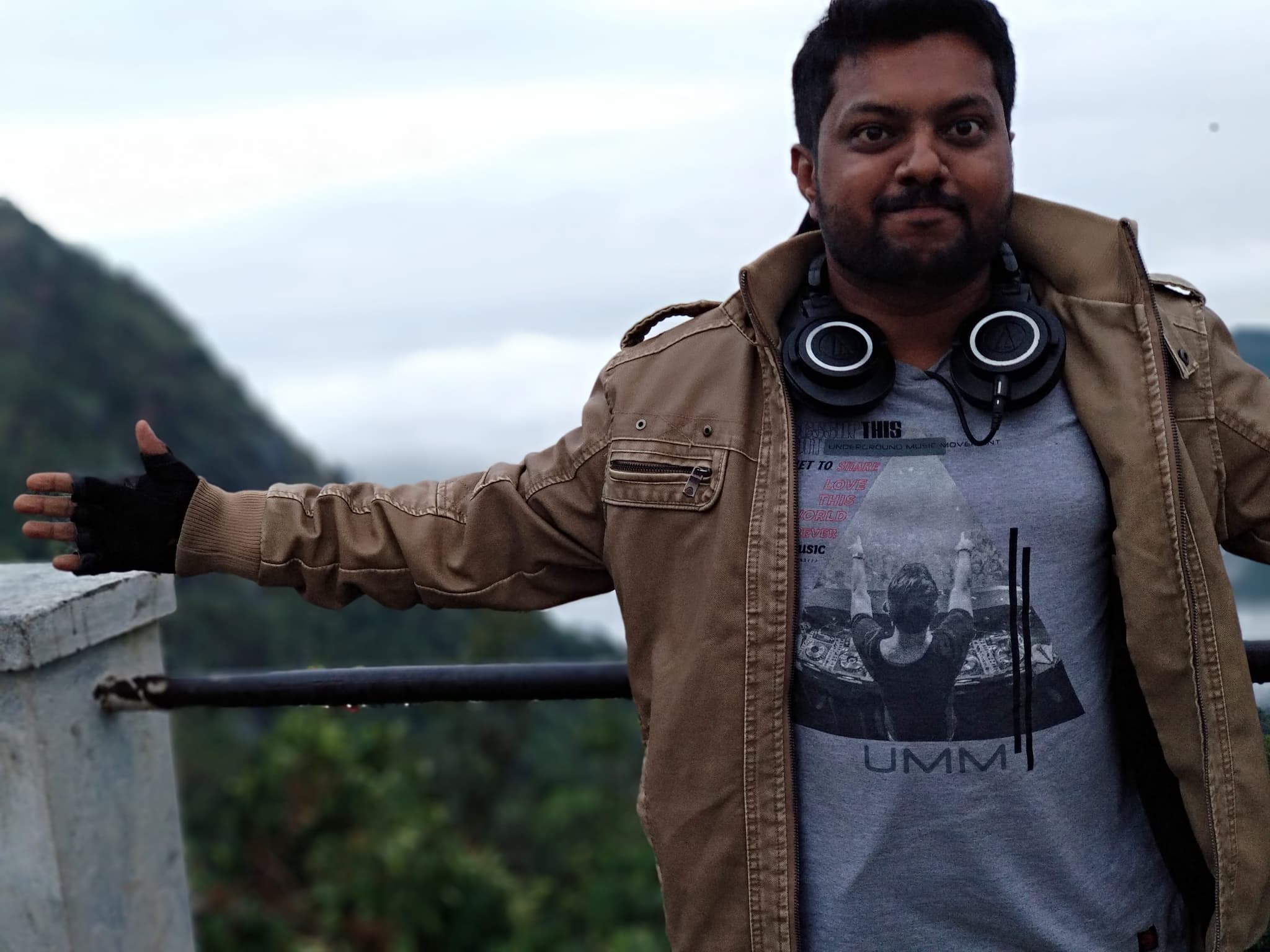 Portrait of a man in a jacket at a mountain viewpoint with clouds and peaks behind