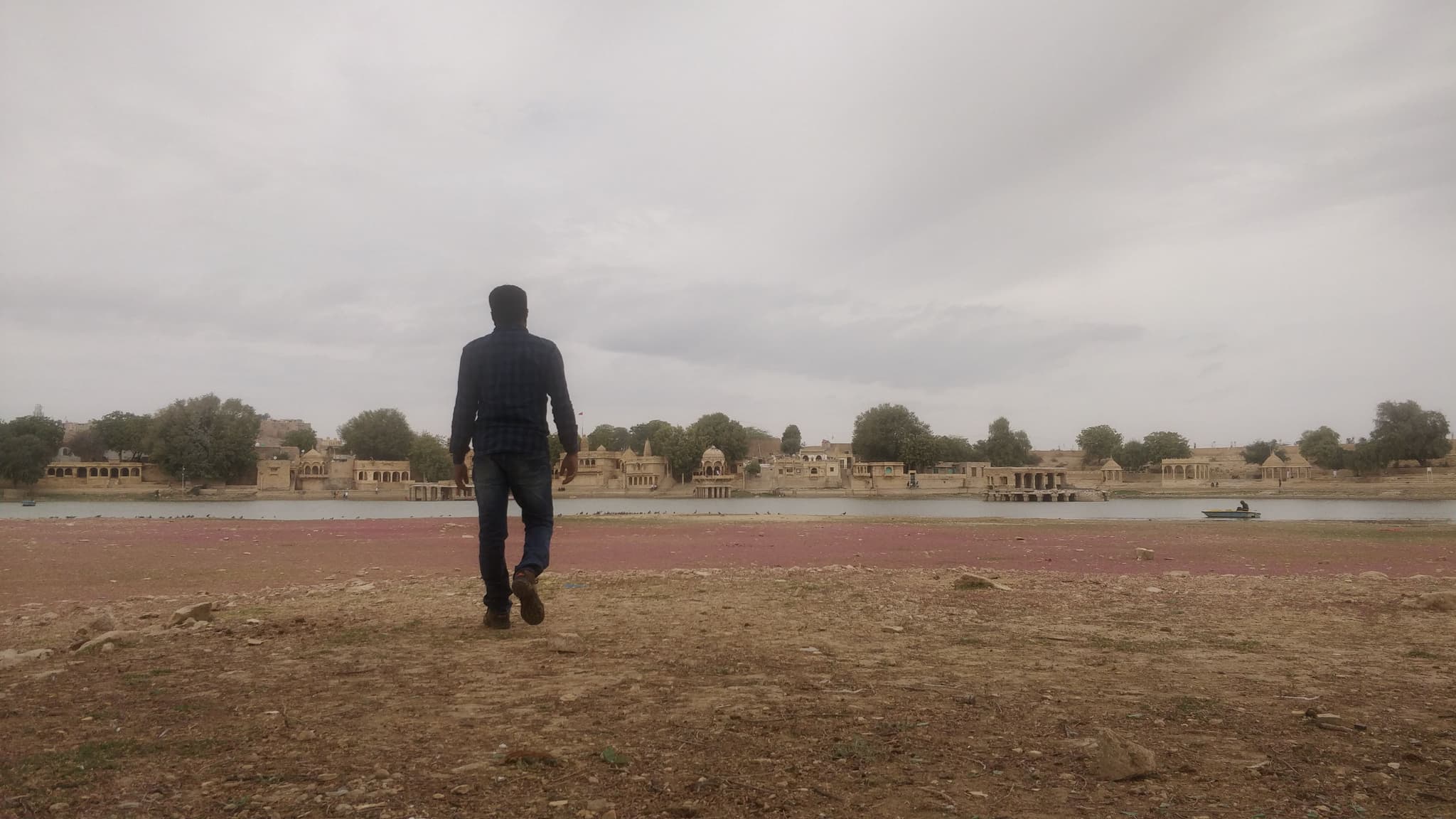 Person walking toward Gadisar Lake with Jaisalmer temples across the water